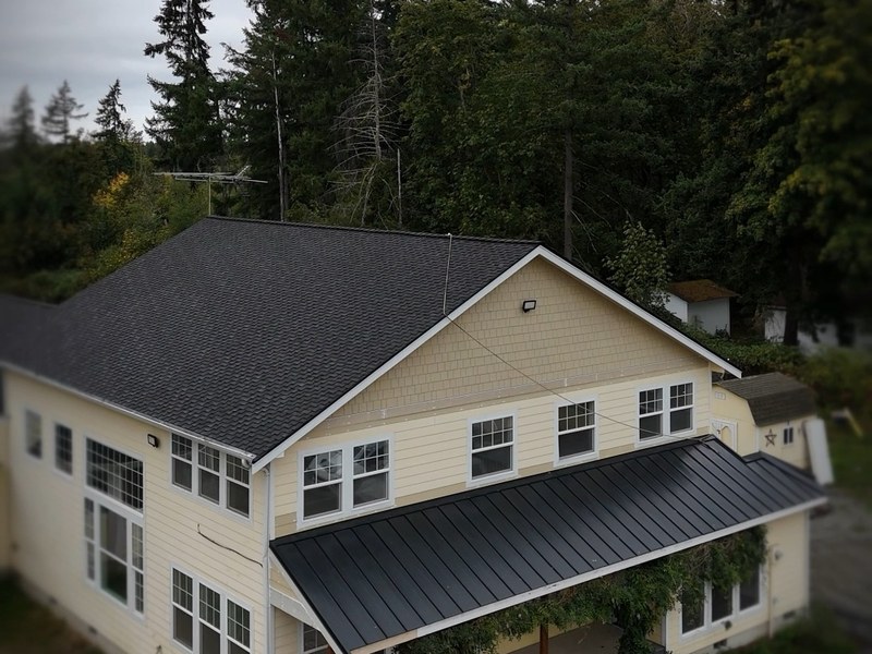 Drone view of a two story house with a new dark shingle roof under a grey Pacific Northwest sky